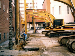Construction vehicles in town alley digging a hole.
